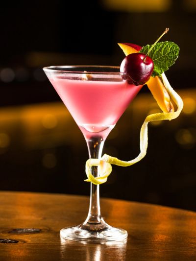 Elegant pink cocktail garnished with cherry, mint, and lemon twist in a martini glass.