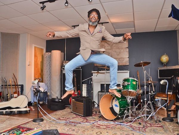 Man joyfully jumps in a music studio filled with instruments.