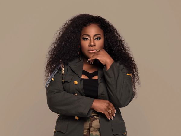 Confident woman with curly hair in military-inspired jacket poses thoughtfully.