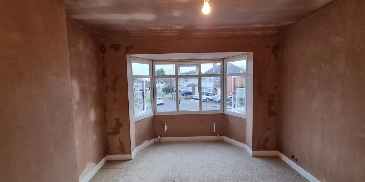 Empty room with freshly plastered walls and large bay windows.