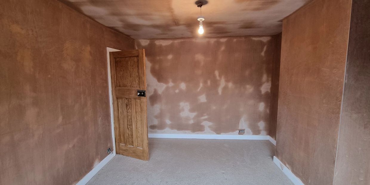 Empty room with freshly plastered walls and an open wooden door.