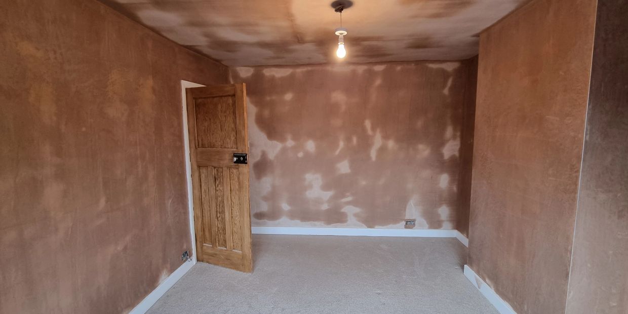 Empty room with freshly plastered walls and an open wooden door.
