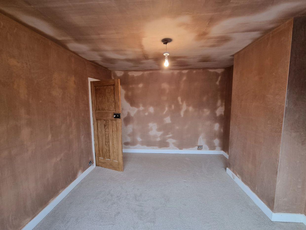 Empty room with freshly plastered walls and ceiling, bare light bulb, and carpeted floor.