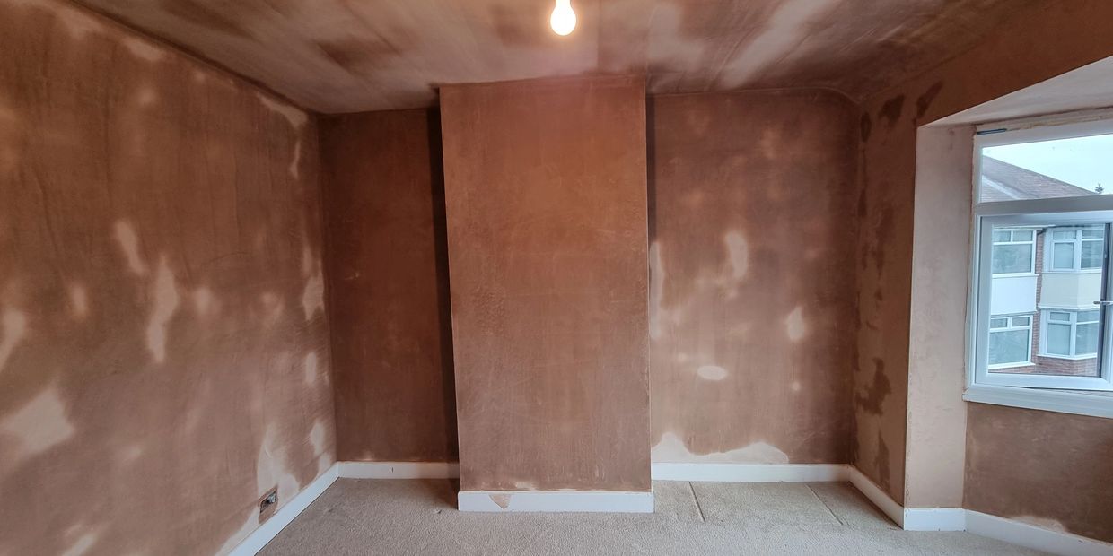 Empty room with freshly plastered walls and a window showing neighboring houses.