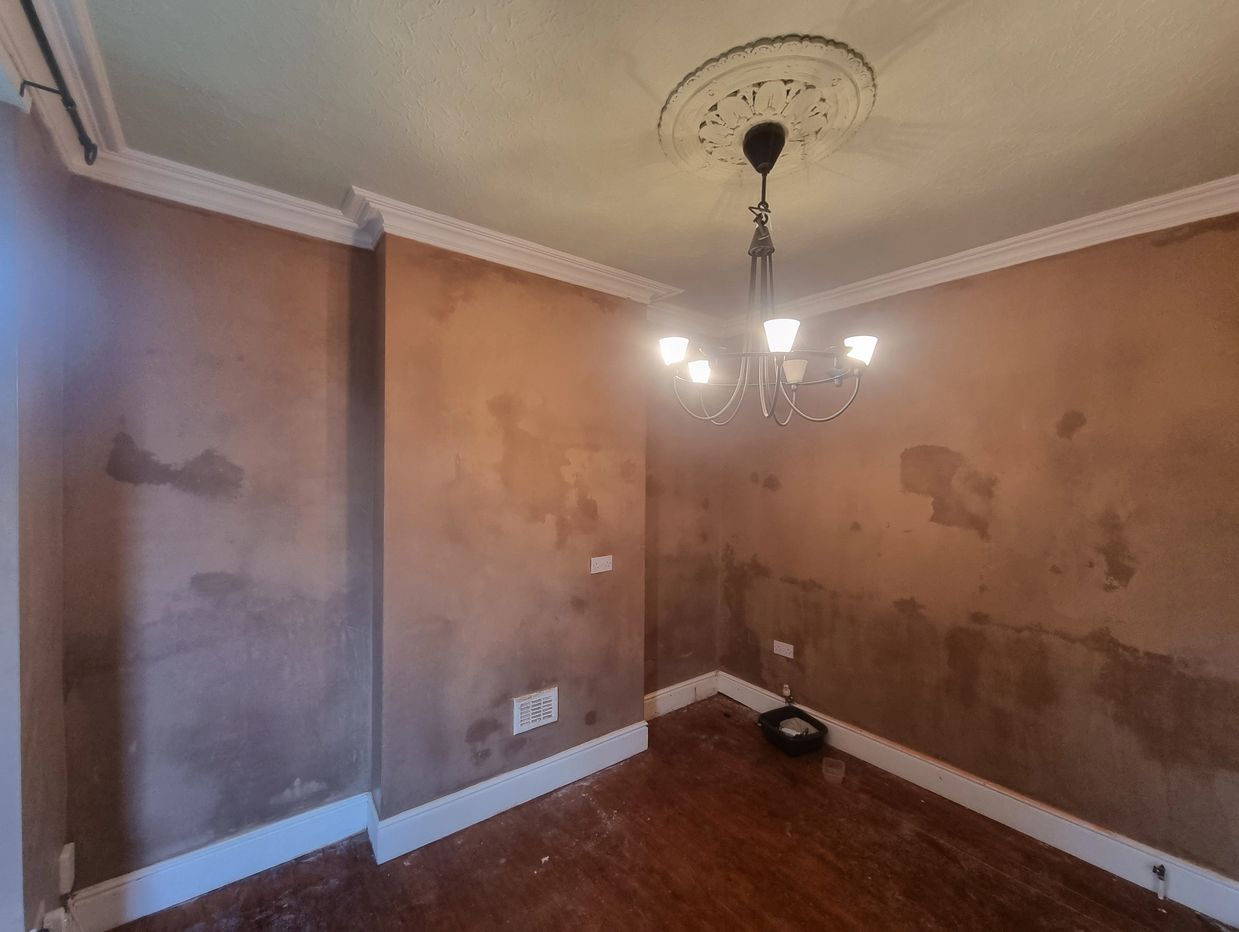 Empty room with unfinished plaster walls and a chandelier hanging from the ceiling.