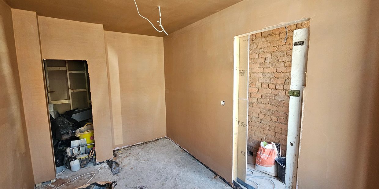 Room under construction with plastered walls and unfinished floor.