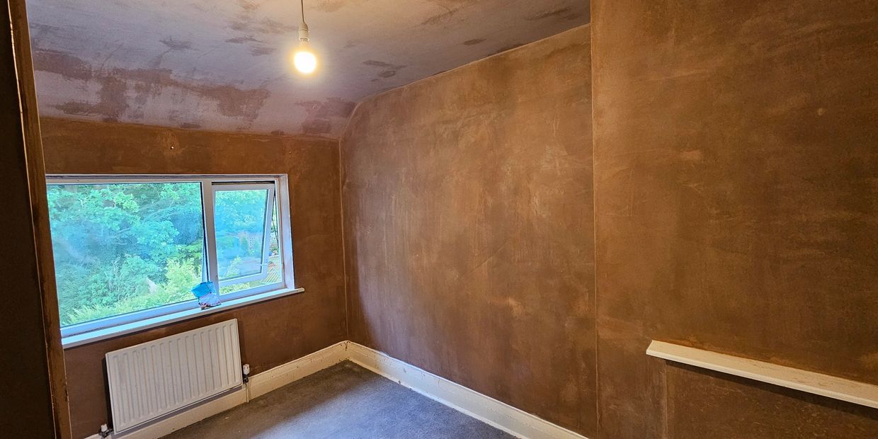Empty room with freshly plastered brown walls and a single light bulb.