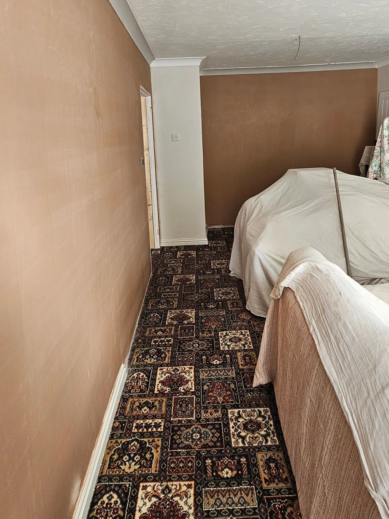 Room with brown walls, patterned carpet, and furniture covered by sheets.