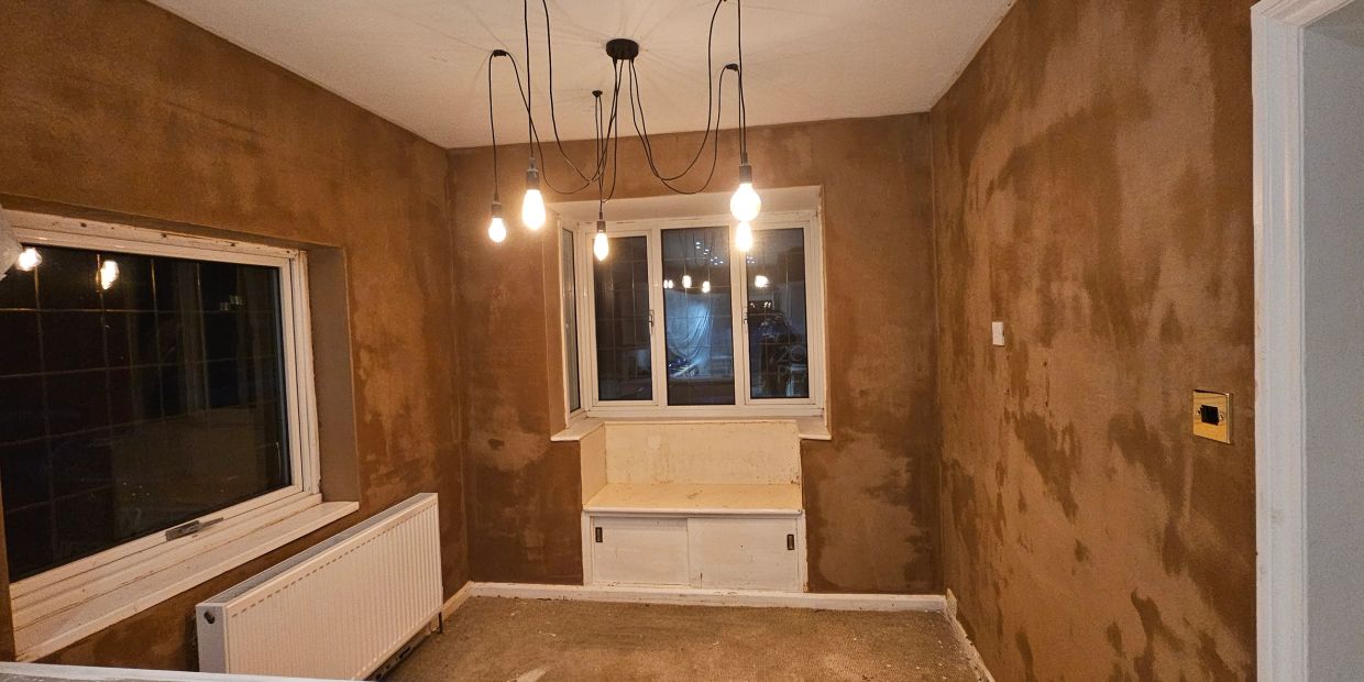 Room with freshly plastered walls and hanging light bulbs.