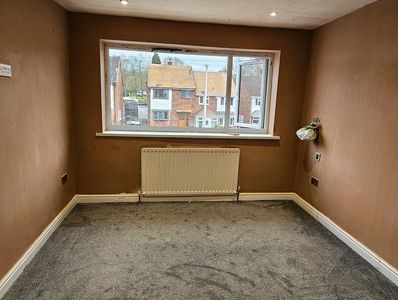 Empty room with brown walls, gray carpet, and a window overlooking houses.