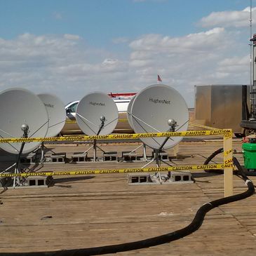 A row of satellite dishes on a rooftop against a partly cloudy sky.
