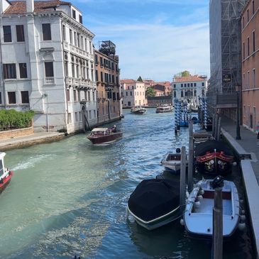 Boats docked along a Venetian canal under a clear blue sky.