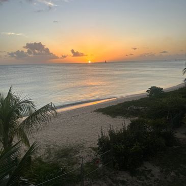 Sunset over a calm beach with a sailboat on the horizon.