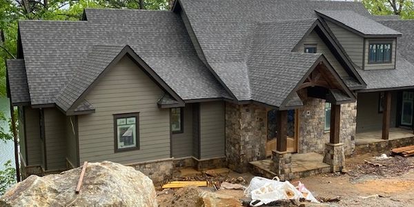A modern house under construction with stone and wood exterior.