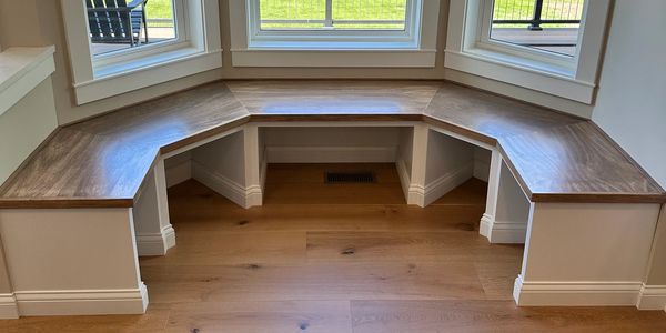 Corner window bench seat with wooden top and white base.