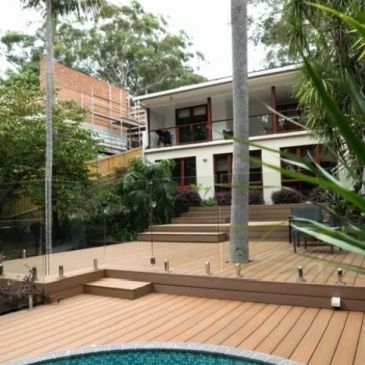 Modern backyard with a pool and wooden deck surrounded by lush greenery.
