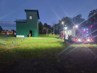 Fire truck and personnel near a green training building at night.