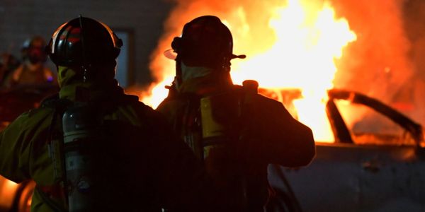 Firefighters facing a blazing car fire at night.