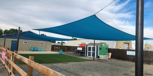 Outdoor shaded seating area with blue tarp canopies and gravel ground.