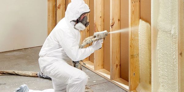 Worker spraying foam insulation onto wooden wall studs.