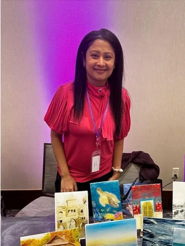 Woman presenting various colorful paintings on a table.