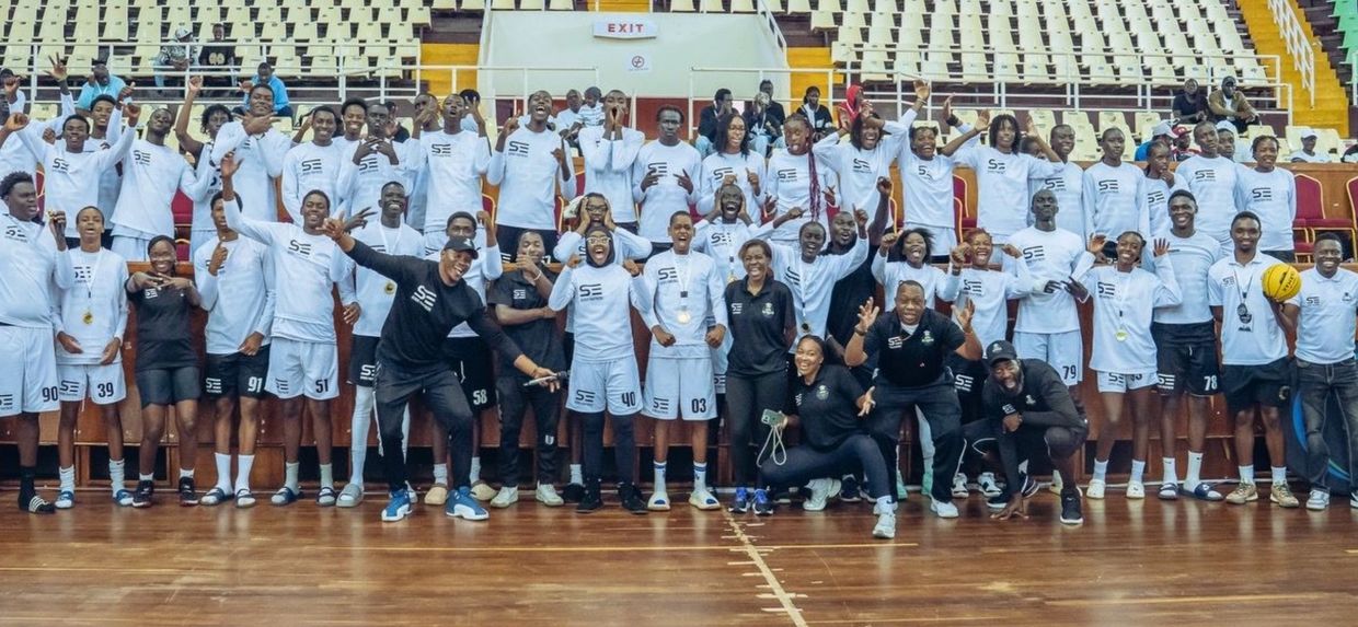 Large group of basketball players and coaches posing happily indoors.