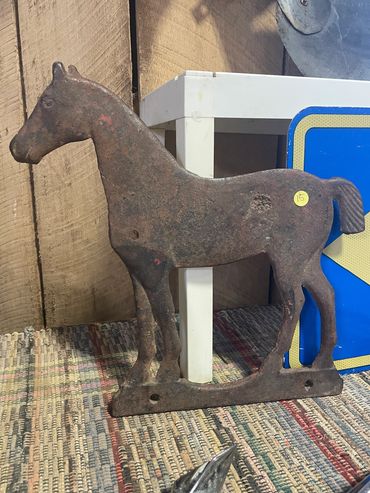 Rusty metal horse silhouette sculpture on a textured surface.