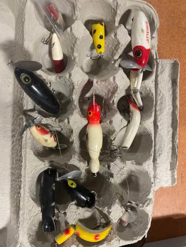 A collection of vintage fishing lures in a cardboard egg carton.