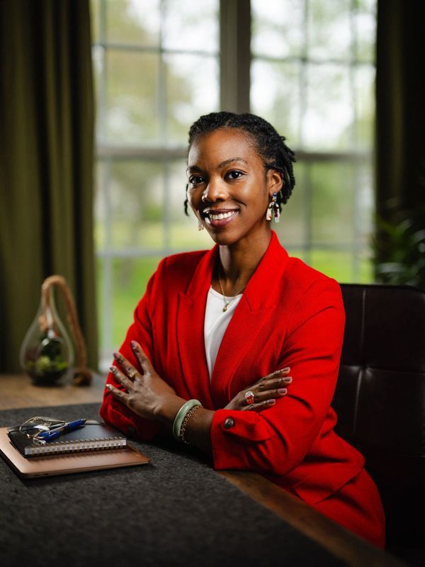 Confident woman in red jacket smiling at desk.