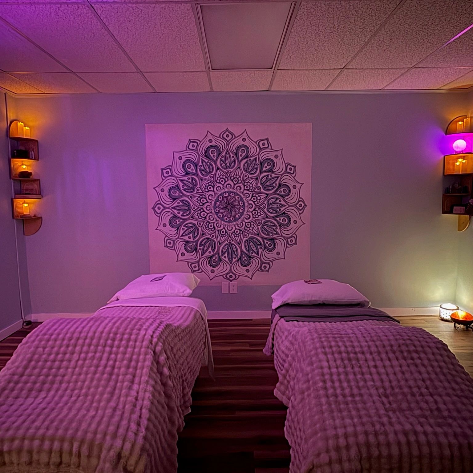 A calm massage room with two beds and soft purple lighting.