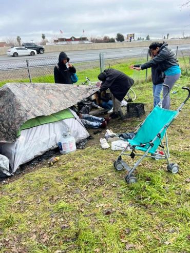 People outside a small tent near a roadside.