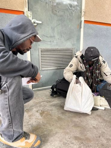 Two people sitting on the ground with bags and papers.