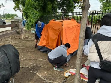 People setting up an orange tent outdoors.