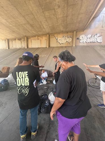 People gathered under a bridge, some giving food or aid.
