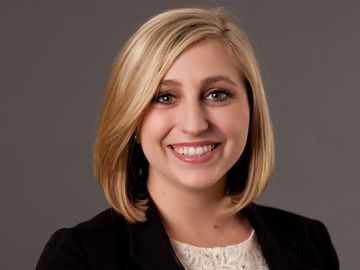 Headshot of a smiling woman with a dark background.