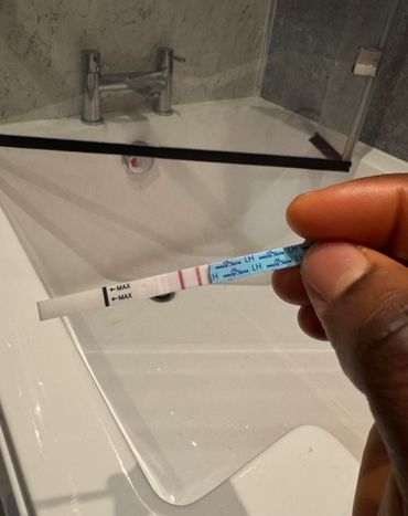 Hand holding a pregnancy test strip over a bathroom sink.