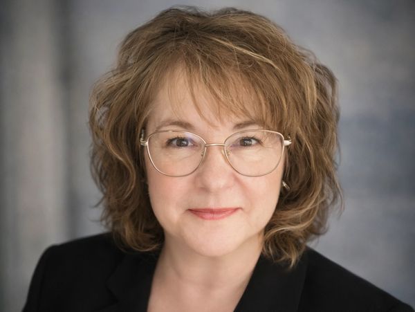 Smiling woman with glasses and wavy hair in a black blazer.