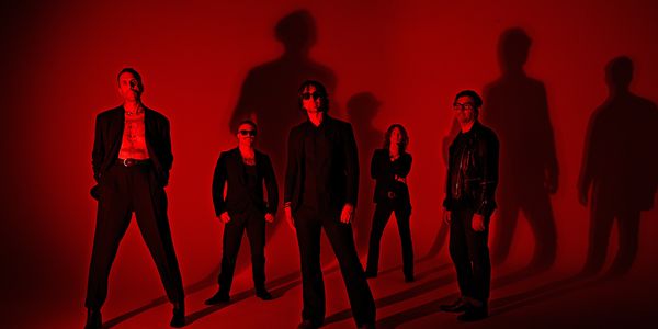 The Killers band members posing in front of a red backdrop, promoting their new album.
