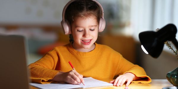 Young girl in front of laptop with headphones on at her desk.