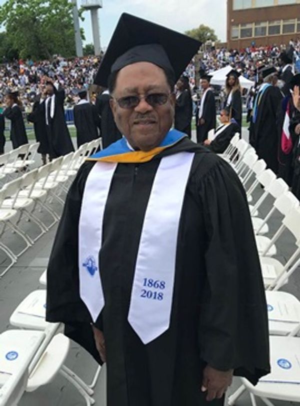 Graduate in cap and gown at a commencement ceremony outdoors.