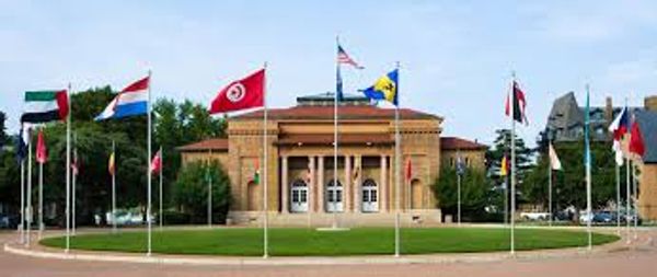 Flags of various countries displayed on flagpoles in front of a classical building.