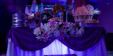 Mesa decorada con flores, pan y objetos dorados en luz morada.