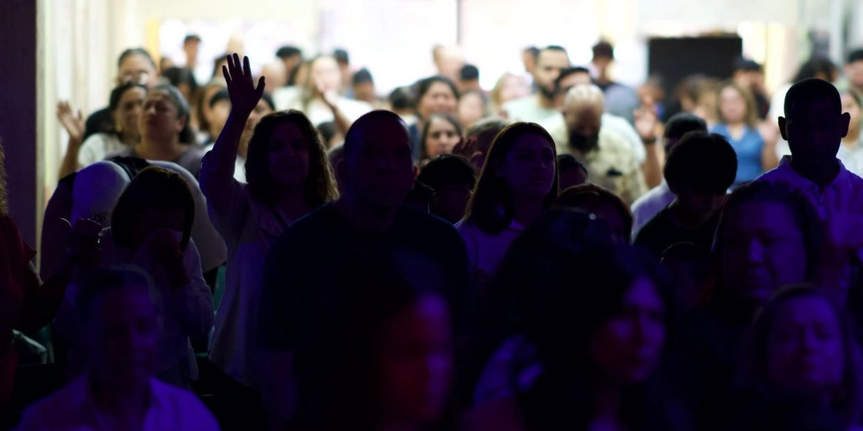 Multitud de personas en un espacio oscuro, algunas con manos levantadas.