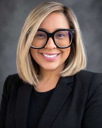 Smiling woman with glasses and blonde hair in black blazer.