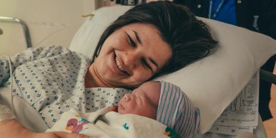 A woman lying in a hospital bed, holding a baby and smiling. Labour and birth doula support.