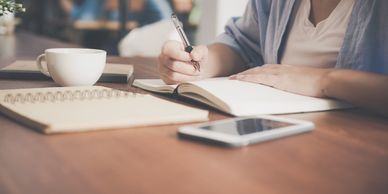 A person sitting at a desk, writing in a notebook. Virtual doula support.