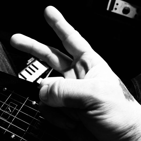 Black and white photo of a hand making a gesture over a guitar neck.