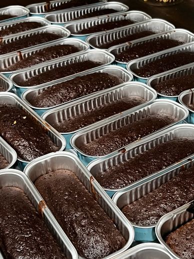 Multiple freshly baked chocolate cakes in rectangular aluminum trays.