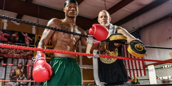 Two men posing in a boxing ring with gloves and pads.