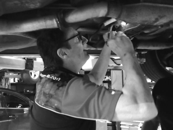 George Bonola repairing a car's underside in a workshop.
